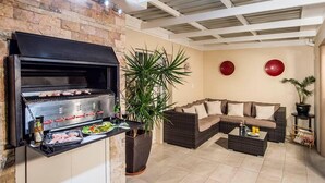 A modern living room with a built-in grill, a large potted plant, a sectional sofa, and a coffee table. - Bhotani Bed and Breakfast (Gqeberha (Port Elizabeth))