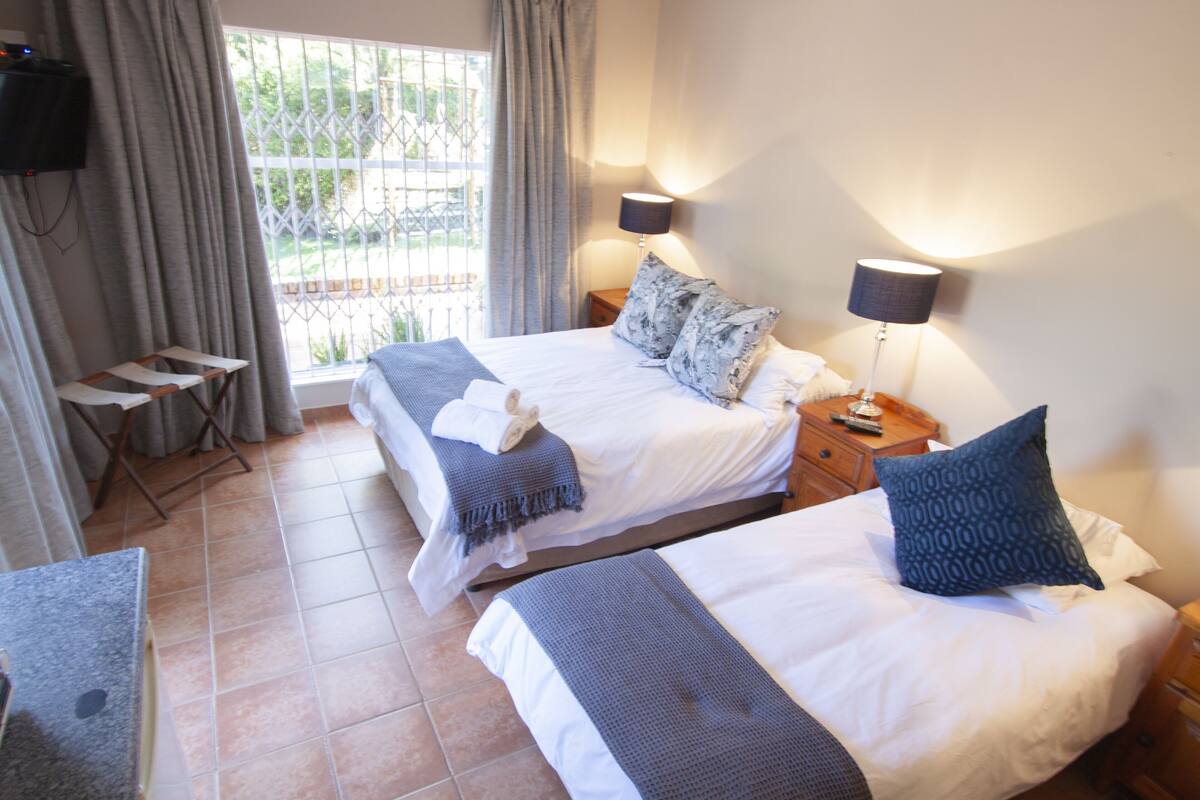 A hotel room with two beds, a TV mounted on the wall, and a window with curtains.