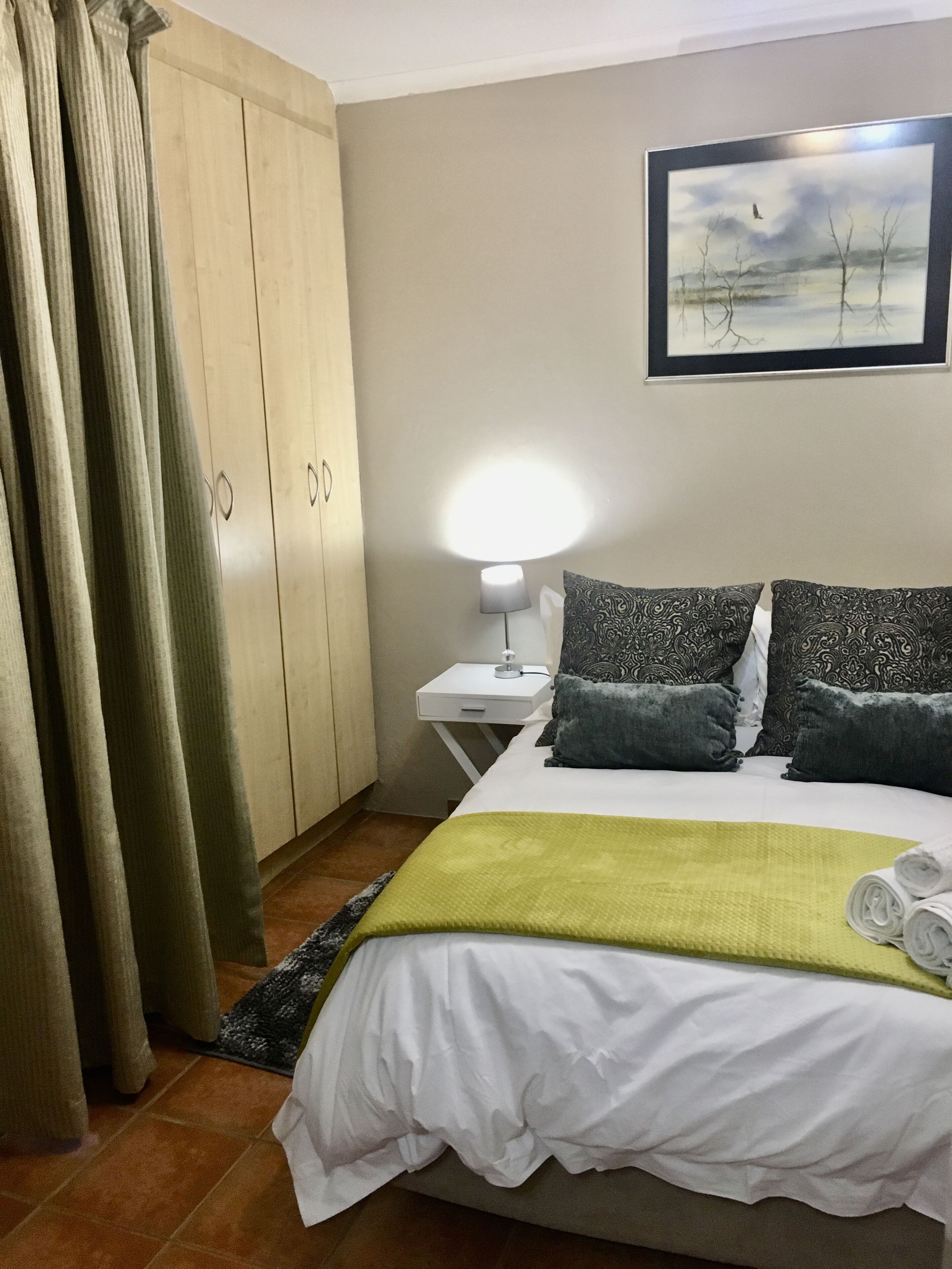 A hotel room with a bed, a nightstand, a lamp, a painting, and a wardrobe.