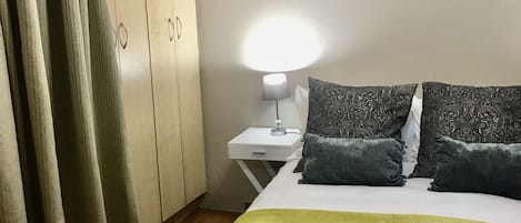 A hotel room with a bed, a nightstand, a lamp, a painting, and a wardrobe.