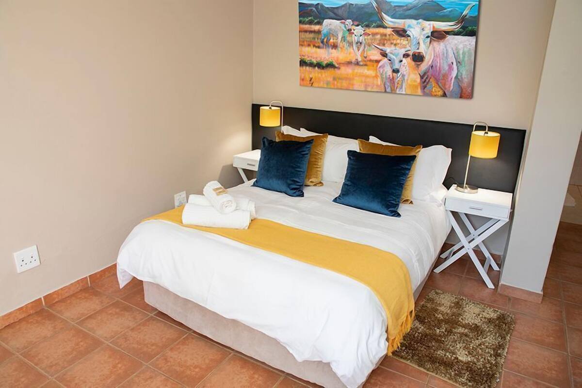 A neatly made bed with white and yellow bedding, two blue pillows, and a brown rug on the floor.
