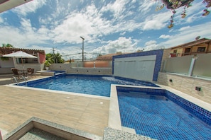 A swimming pool with blue tiles, a tiled deck, and a patio area with chairs. - Hotel Tuareg (Porto Seguro)