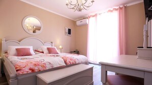A bedroom with a bed, bedside tables, a mirror, an air conditioning unit, and a window with curtains. - Prestige Rooms (Zadar)