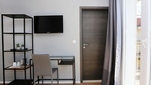 A room with a TV mounted on the wall, a desk with a chair, a bookshelf, and a door. - Prestige Rooms (Zadar)
