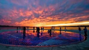 A circular plaza with a reflective floor, surrounded by a body of water and a sunset sky. - Prestige Rooms (Zadar)