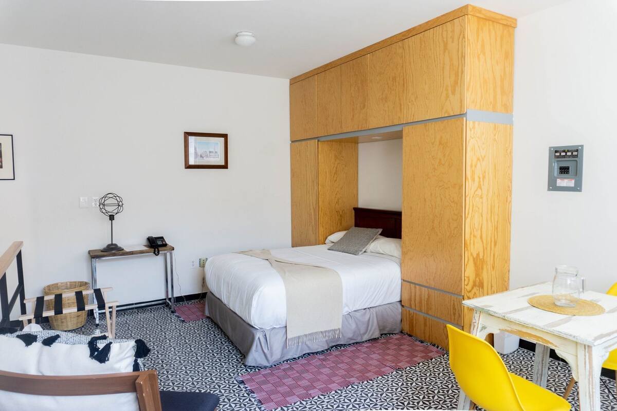 A bedroom with a bed, bedside table, lamp, chair, and a small table with a glass.