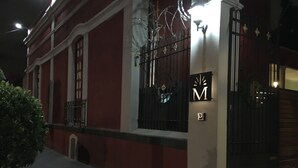 A building with a red facade, a black gate, and a sign with a capital 'M'. - Casa Moctezuma (Mexico City)