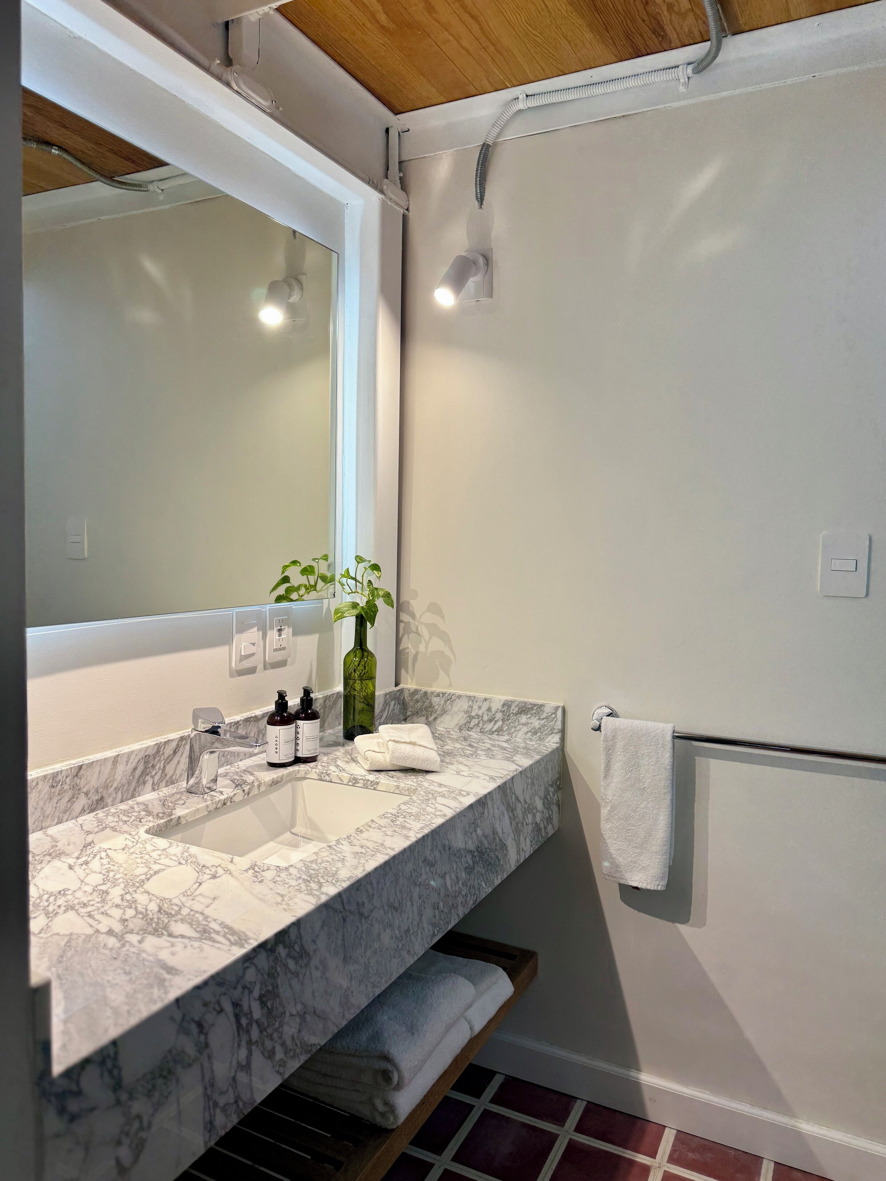 A bathroom with a marble sink, a mirror, a towel rack, and a shower area.