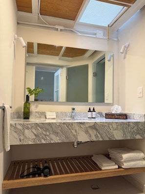 A bathroom with a marble countertop, a large mirror, a green bottle, and a towel rack. - Casa Moctezuma (Mexico City)