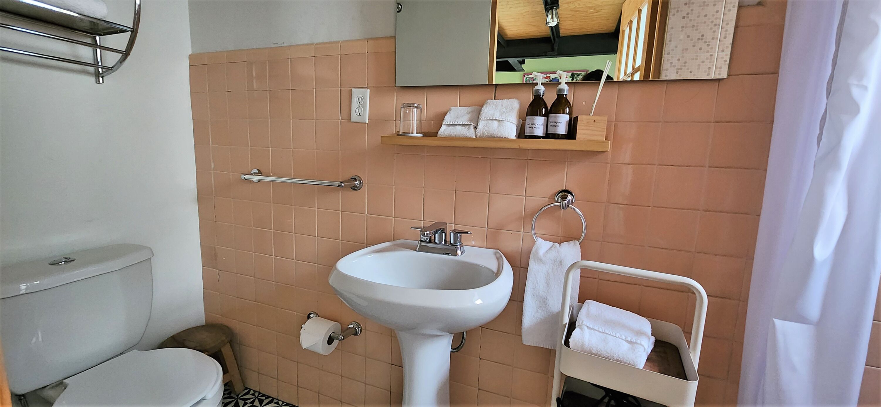 A bathroom with a white sink, a towel rack, a toilet, and a shelf with toiletries.