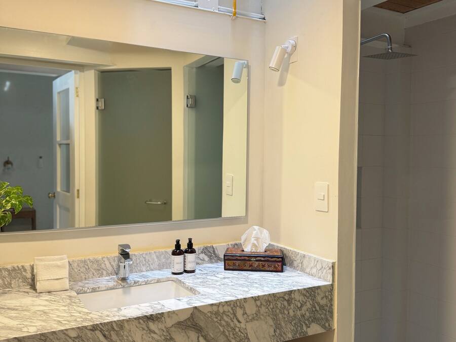 Un baño moderno con encimera de mármol, un espejo grande, un perchero y una zona de ducha.