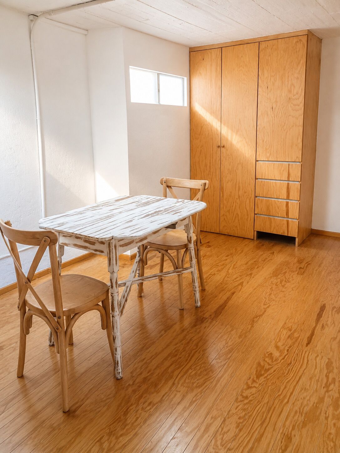 A room with a wooden table and chairs, a wardrobe, and a window.