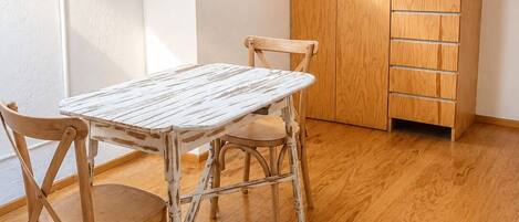 A room with a wooden table and chairs, a wardrobe, and a window.