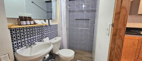 A bathroom with a white sink, a toilet, and a shower area with a patterned tile wall.