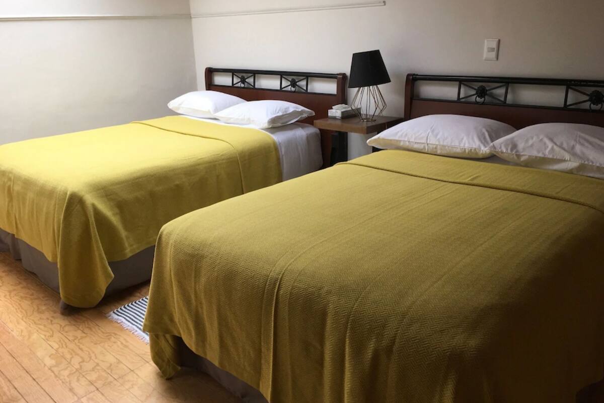 Two single beds with yellow bedding, a bedside table with a lamp, and a wooden floor.
