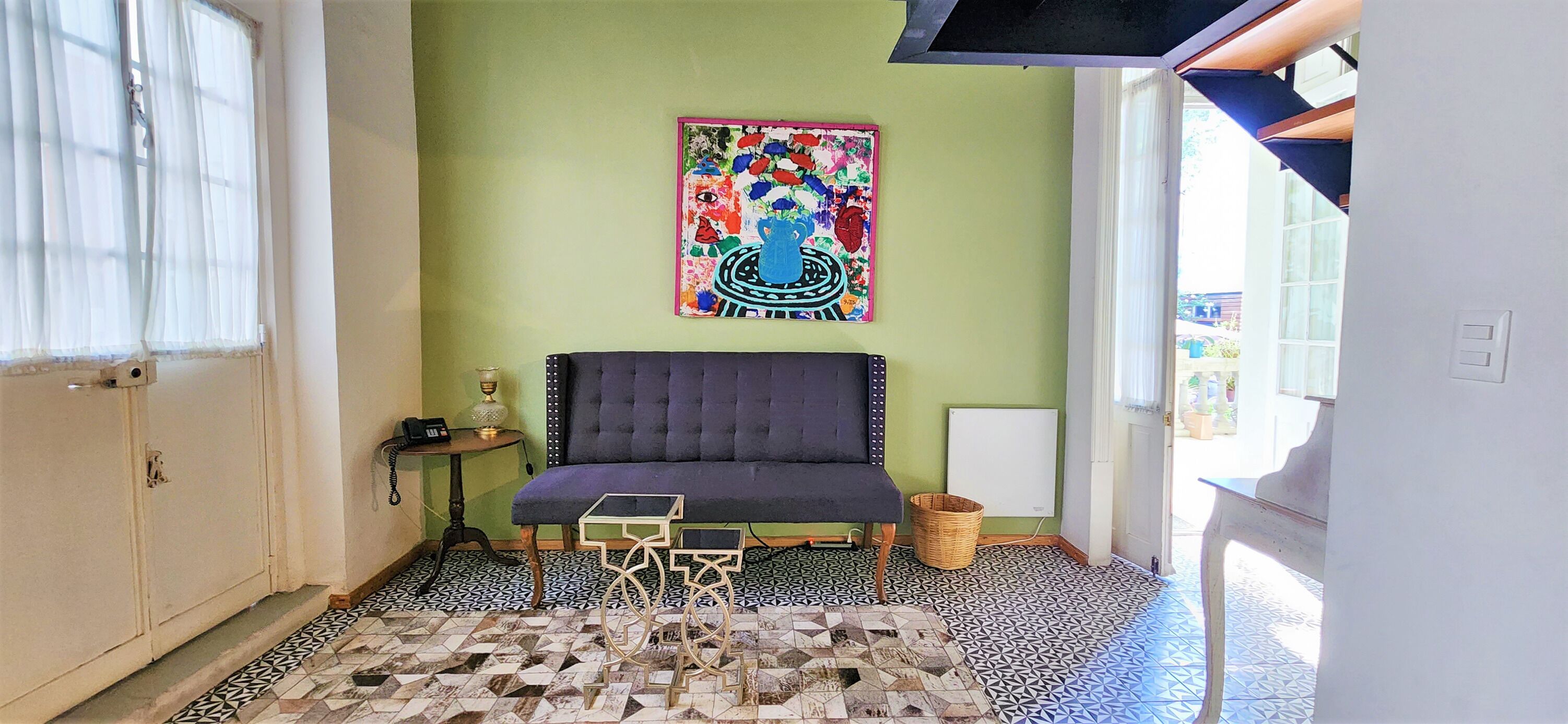Een kamer met een bank, een kamer met een patroon vloer, een muur met een kleurrijk schilderij en een raam met transparante gordijnen.