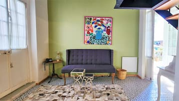 Een kamer met een bank, een kamer met een patroon vloer, een muur met een kleurrijk schilderij en een raam met transparante gordijnen.