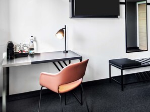 Moderni hotellihuone, jossa on työpöytä, tuoli, pieni pöytä, seinälle asennettu televisio ja ikkuna, josta on näkymä ulos.