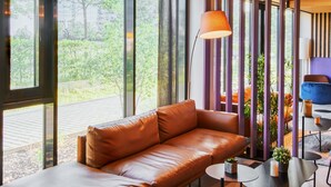 A modern living room with a leather sofa, a small round table, and a blue chair. - B&B Hotel Frankfurt-Airport (Frankfurt)