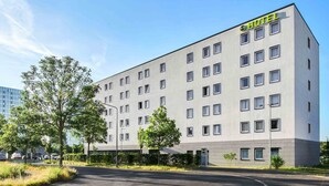 A modern hotel building with a flat facade, multiple windows, and a parking area in front. - B&B Hotel Frankfurt-Airport (Frankfurt)