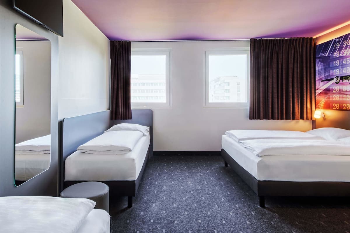 A hotel room with two beds, a round table, a large mirror, and a wall clock.