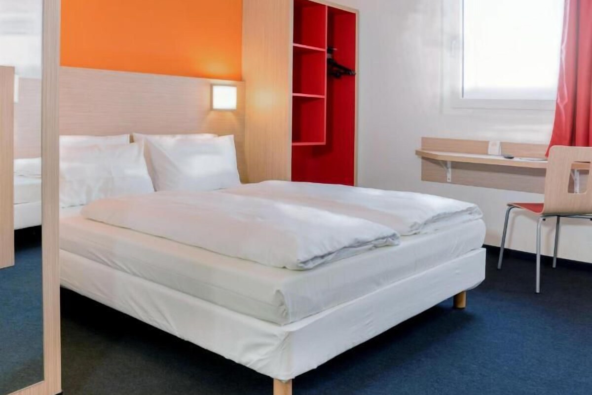Una camera d'albergo con un letto, una scrivania, una sedia e un armadio.