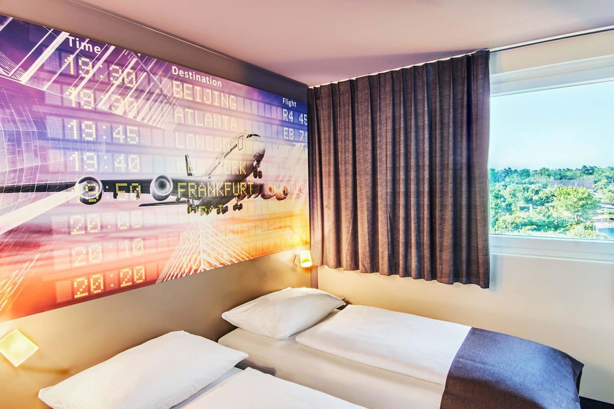 A hotel room with a bed, a window with curtains, and a wall displaying flight information.