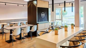 Eine moderne Hotelhalle mit einer langen Rezeption, mehreren Tischen und Stühlen und großen Fenstern mit Blick ins Freie.