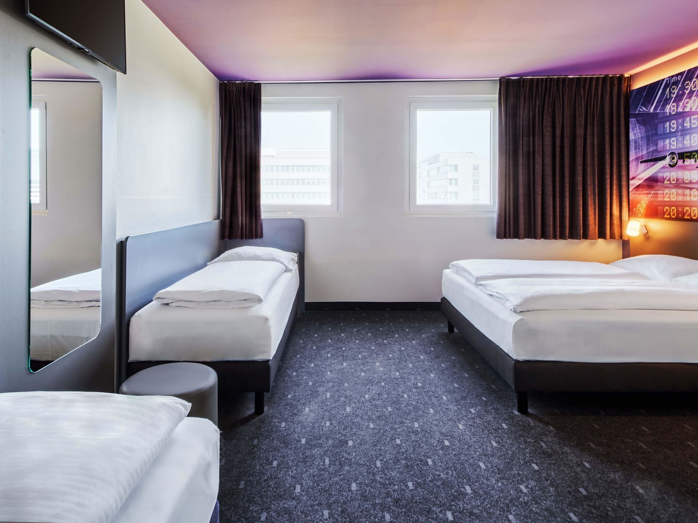 Ett hotellrum med två sängar, ett runt bord, en stor spegel och en väggklocka.