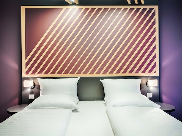Quarto de hotel com uma cama grande, duas mesas de cabeceira com luminárias e um papel de parede estampado atrás da cama.