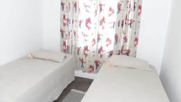 A room with two single beds, a window with patterned curtains, and a plain white wall.