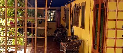 A covered patio area with tiled flooring, wooden furniture, and potted plants.