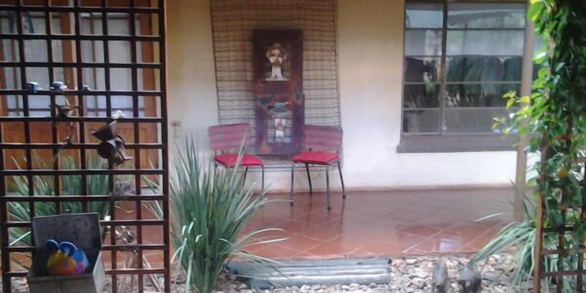 A covered patio area with a tiled floor, two red chairs, a small table, and a decorative wall.