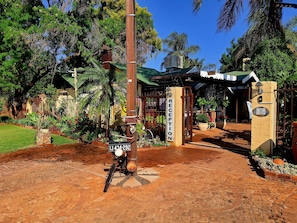 A reception area with a sign reading "RECEPTION," a motorcycle parked in front, and a gate leading to a building with a green roof. - Africa s Eden Guesthouse (Mookgopong)