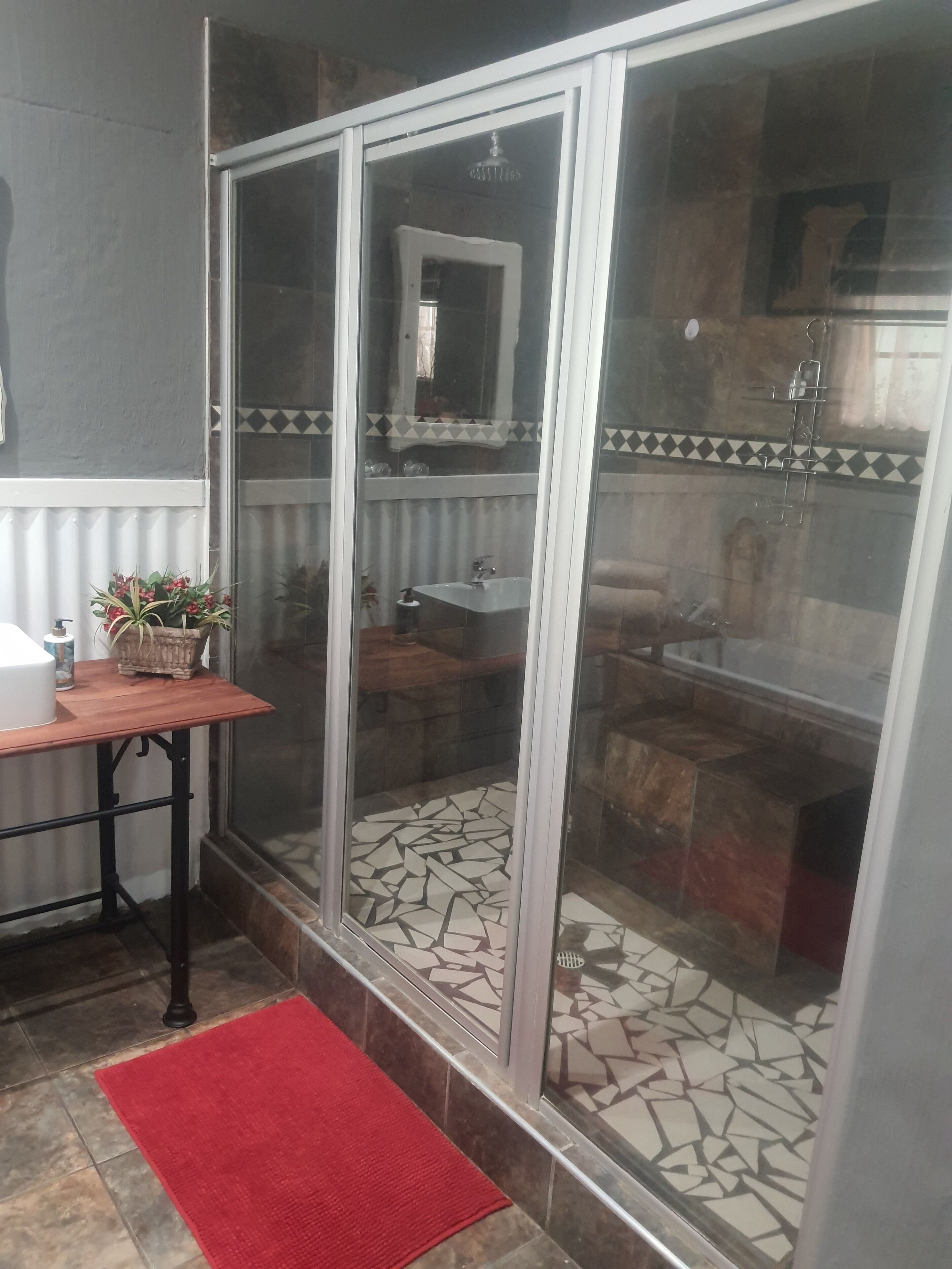 A bathroom with a glass shower enclosure, a sink, and a mirror.
