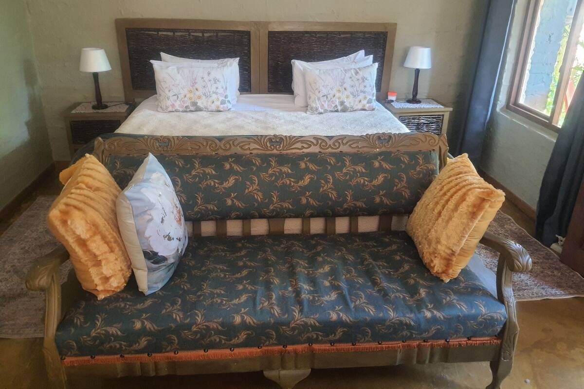 Un lit double avec une literie à motifs floraux, deux lampes de chevet et un canapé agrémenté de coussins à motifs.