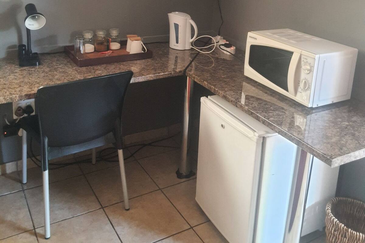 Une cuisine compacte équipée d’un four à micro-ondes, d’une bouilloire et d’un petit réfrigérateur. On peut également y voir une chaise et une table.