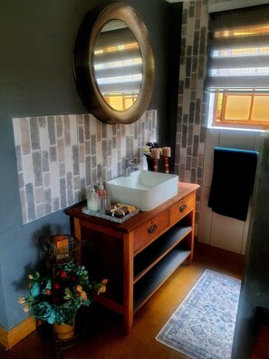 A bathroom with a white sink, wooden vanity, and a mirror. There is a window with blinds, a towel hanging on the wall, and a decorative plant. - Africa s Eden Guesthouse (Mookgopong)