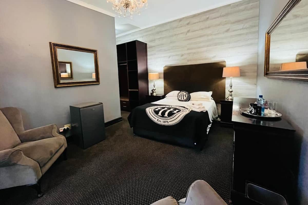 A hotel room with a large bed, a desk, a chair, a wardrobe, and a chandelier.