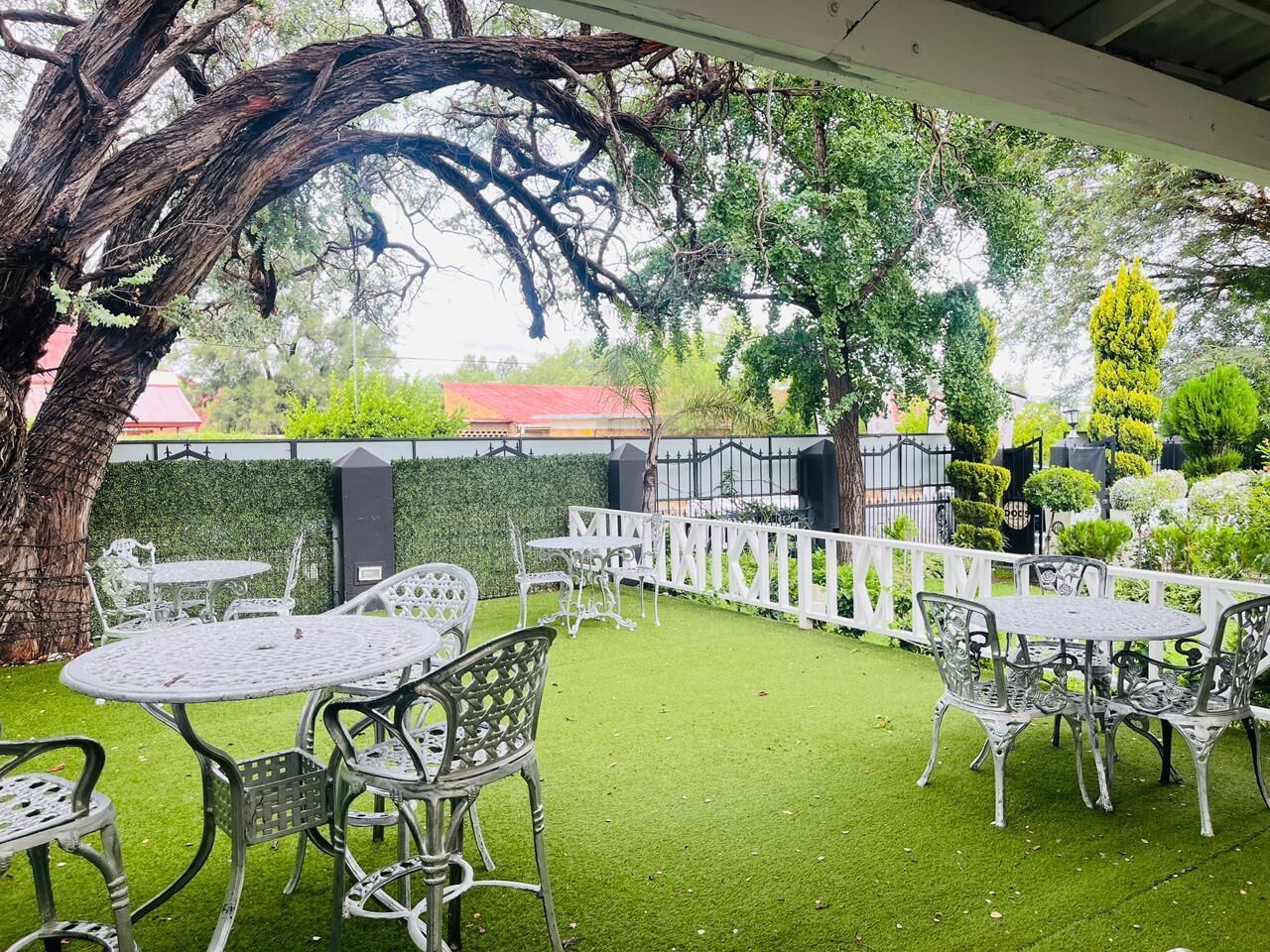 An outdoor patio area with tables and chairs, surrounded by a white fence and greenery.