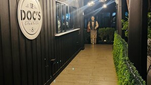 Ein Korridor mit Holzwänden, einem Schild für das Café 'DOC'S Coffee & Tea' und hängenden Pendelleuchten.