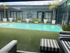 Una piscina con césped artificial, sillas de descanso y plantas en macetas.