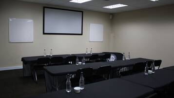 A conference room with a projector screen, whiteboards, tables, chairs, and water bottles.