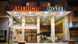 The exterior of the America Hotel with a prominent sign, large columns, and a reception area visible through the glass doors. - America Hotel (Mar del Plata)