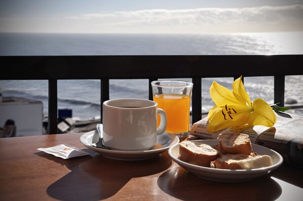 A table with a cup of coffee, a glass of orange juice, a plate with bread, and a yellow flower.