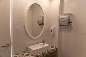 A bathroom with a white sink, an oval mirror, and two paper towel dispensers. - Kings Hotel (Mar del Plata)