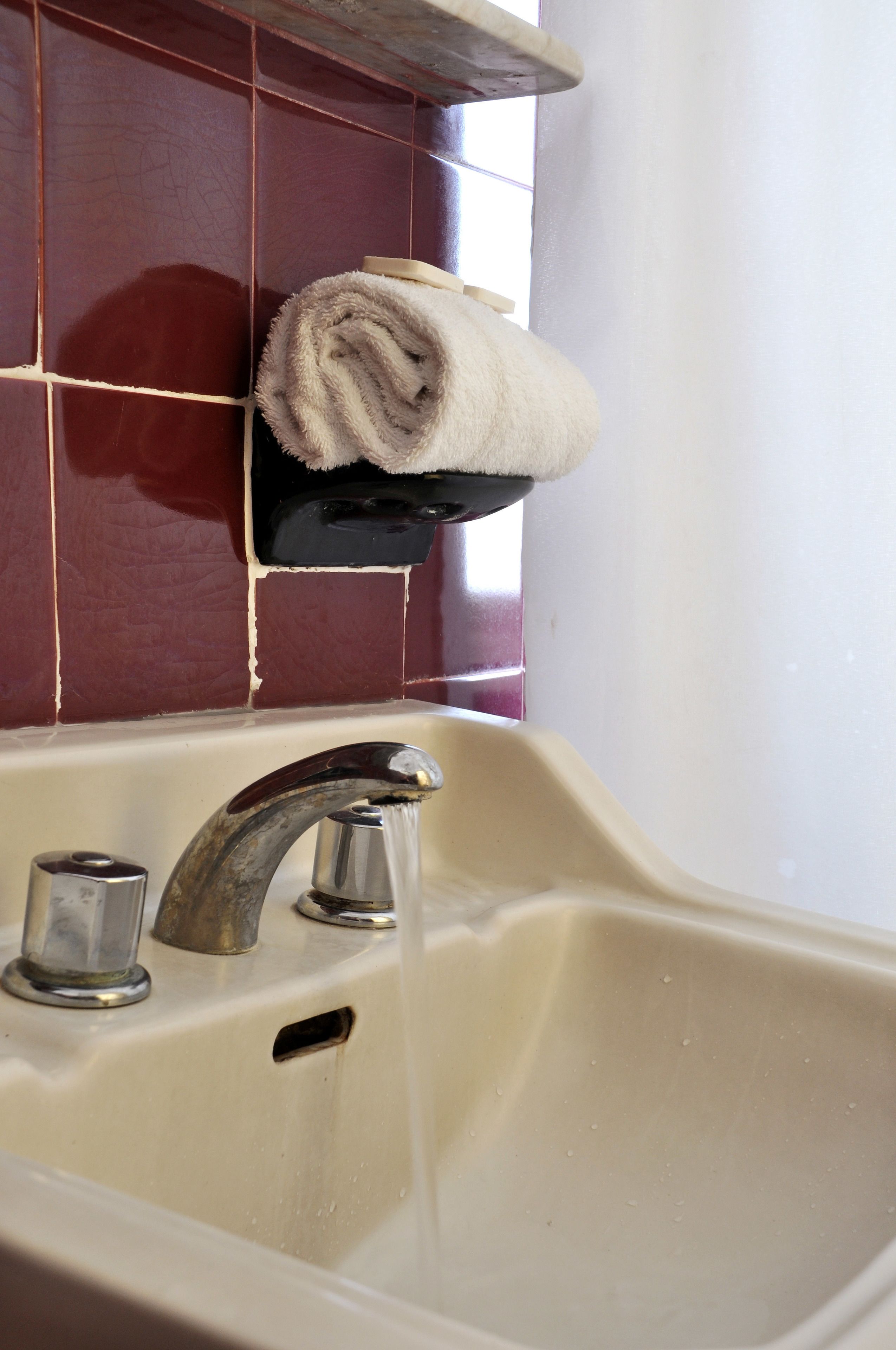 A bathroom sink with running water, a towel rack with a rolled towel, and a tiled wall.