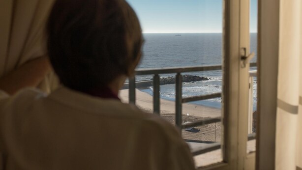 Una persona mirando por la ventana una playa con barandilla.