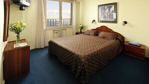 A hotel room with a large bed, a window with a view, a painting on the wall, and a desk with a vase of flowers. - Kings Hotel (Mar del Plata)