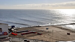 Una playa con vista despejada al océano, una zona arenosa con construcciones y una carretera paralela a la playa.